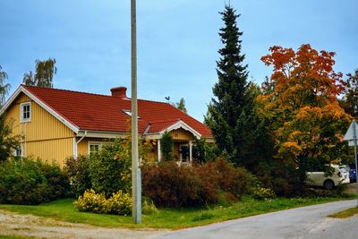 House by road amidst trees and buildings against sky