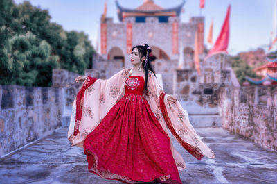 Woman with red umbrella standing against built structure