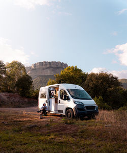 Tourist sitting on chair near caravan car and reading book in mountainous area during road trip in catalonia