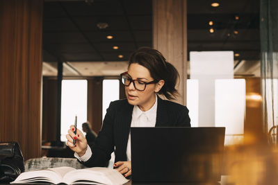 Female lawyer with laptop concentrating while reading book at office