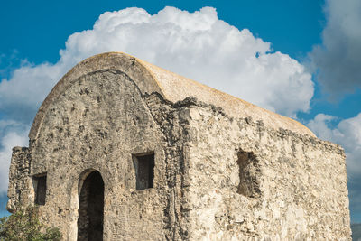 An abandoned greek chapel against a blue sky with clouds is located on a mountain 
