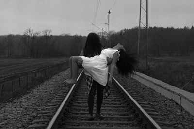Woman carrying friend on railroad track