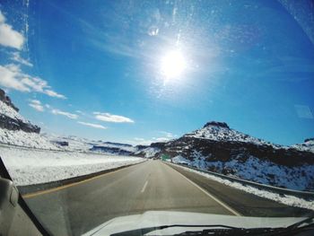 Road amidst snowcapped mountains against sky seen through car windshield