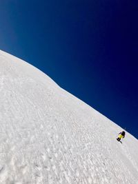 Person on snowcapped mountain against clear blue sky