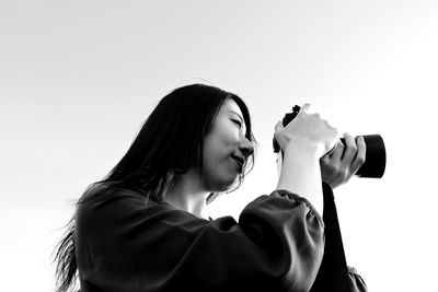 Low angle view of woman photographing against sky