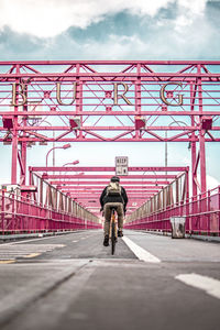 Rear view of man riding bicycle on bridge against sky