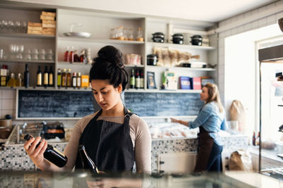 Confident woman checking bottles while colleague standing in background at retail display