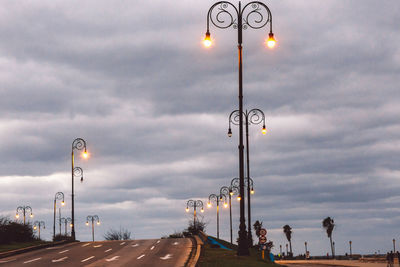 Street lights on road against cloudy sky