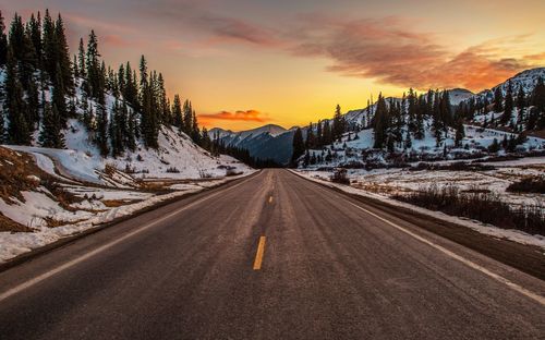 Road amidst snowcapped mountains against sky during sunset