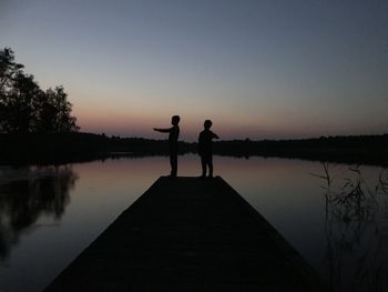 Silhouette people standing on lake against sky during sunset