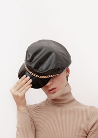 Woman holding hat in front of face against white background