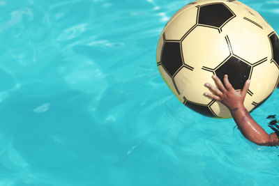 Cropped hand of boy holding ball in swimming pool