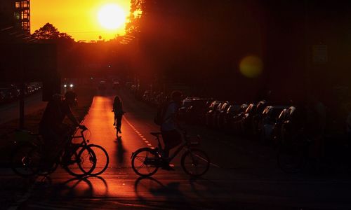Silhouette people riding bicycles on street in city