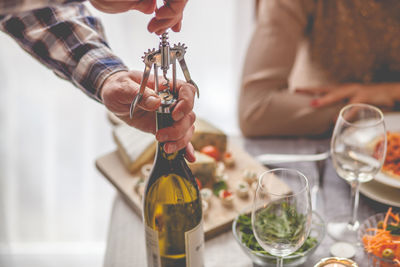 Cropped hand of man using corkscrew on wine bottle