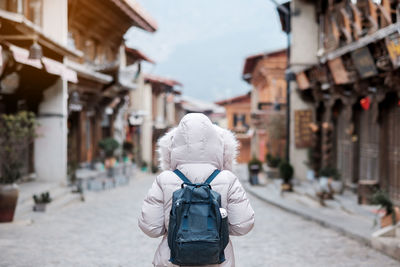 Rear view of woman with backpack standing on road amidst buildings