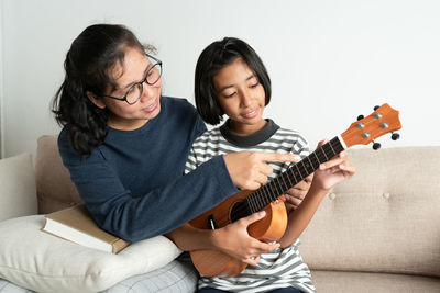 Full length of a girl playing guitar on sofa