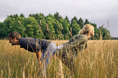 Couple enjoying at grassy field against cloudy sky