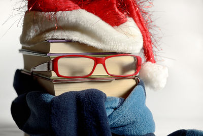 Close-up of stacked books with eyeglasses and santa hat against white background