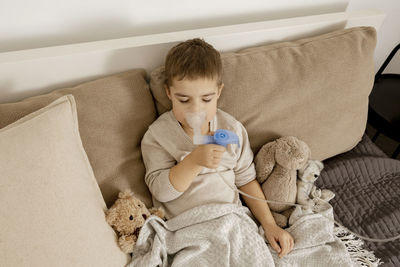 Sick little boy with inhaler for cough treatment. unwell kid doing inhalation on his bed. flu season