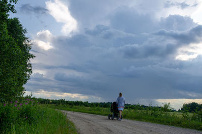 Rear view of woman walking with baby carriage on road against sky