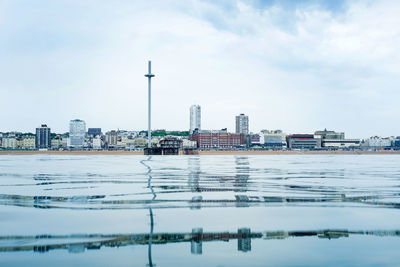 Buildings by river against cloudy sky in city