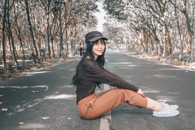 Portrait of young woman on road against trees
