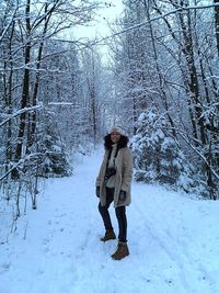 Portrait of woman standing on snow covered land amidst trees