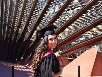 Portrait of smiling young woman standing against a building in graduation robes