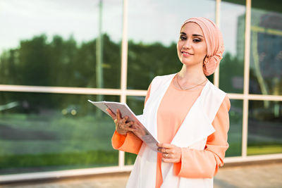 Portrait of woman holding smart phone while standing outdoors