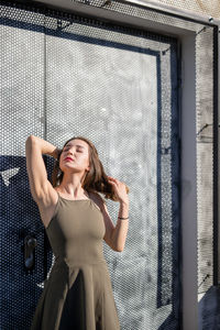 Thoughtful young woman with eyes closed while standing against warehouse