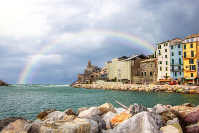 Scenic view of rainbow over sea by buildings against sky