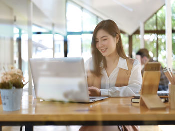 Smiling young businesswoman using laptop while sitting at cafe