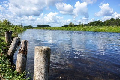 Wooden posts in lake against sky