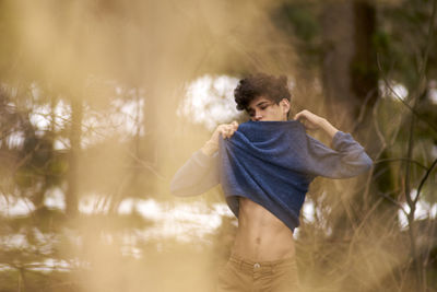 Young man wearing sweater while standing at forest