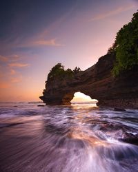 Rock formation in sea against sky during sunset