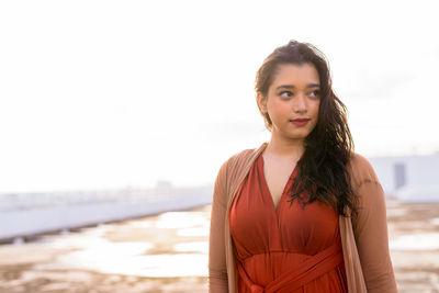 Portrait of young woman standing at beach against sky