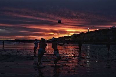 Silhouette people playing at beach against sky during sunset