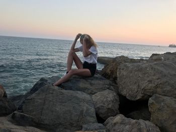 Woman sitting on rock by sea against clear sky