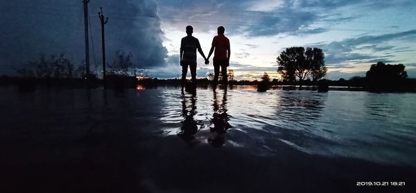 Silhouette people standing by swimming pool against sky during sunset