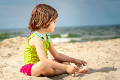 Girl relaxing on sand at beach against sky