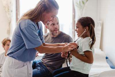 Smiling doctor assisting girl in listening her own heartbeats at hospital