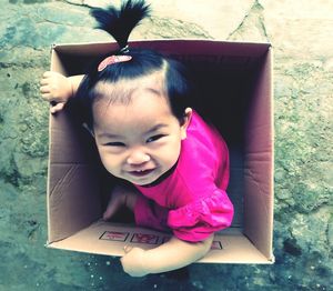 High angle view of cute baby girl sitting in cardboard box