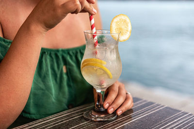 Close-up photo of woman drinking refreshing lemonade on straw in a bar by sea