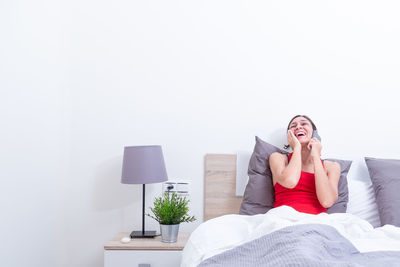 Young woman using mobile phone while sitting on bed at home