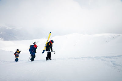 Three friends snowboarders skiers go uphill with a snowboard and skis in their hands for backcountry