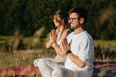 Young adult couple meditating outdoors in the nature, cheerful woman and happy man practicing yoga	
