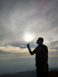 Optical illusion of silhouette man touching sun while standing against cloudy sky during sunset