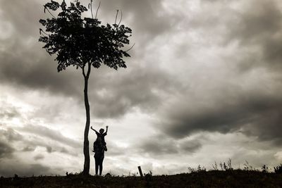 Mother carrying son on shoulders while standing on field against cloudy sky