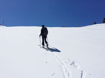 Rear view of person skiing on snow covered field against clear blue sky
