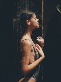 Side view of young woman standing against black background